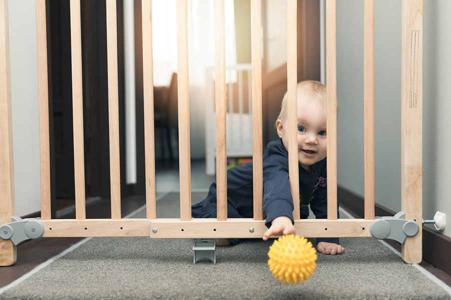 Baby throws a yellow ball through the baby gate on the floor.